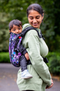 Asian lady carrying a baby in a sling on her back. There are trees in the background.