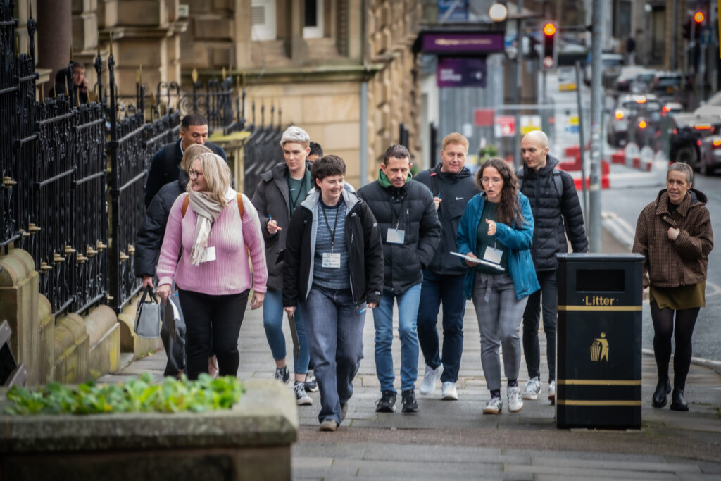 A group of people walking on a street in the town centre. Lady leading the group is holding a clipboard