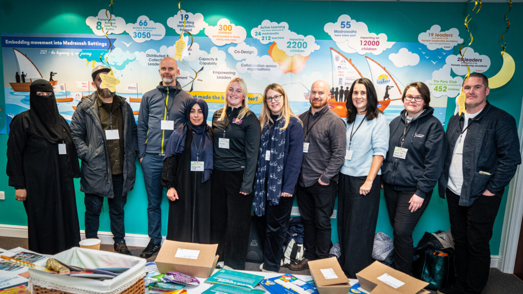 Group of people stood in front of a wall mural titled 'Embedding movement into Madrassah settings'.