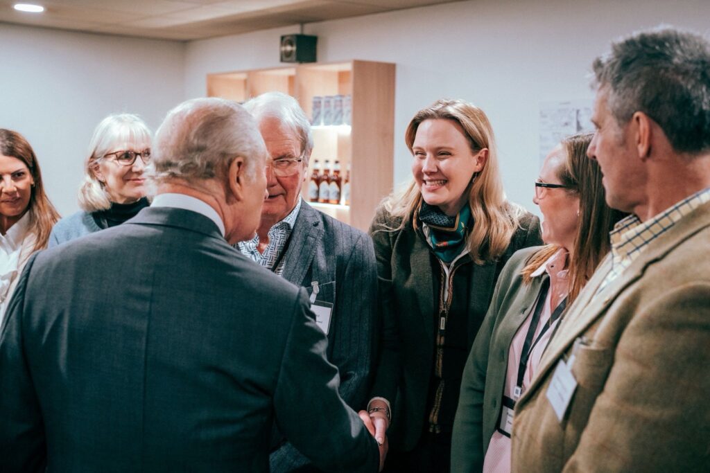 Harriet in group of people, shaking King Charles's hand.